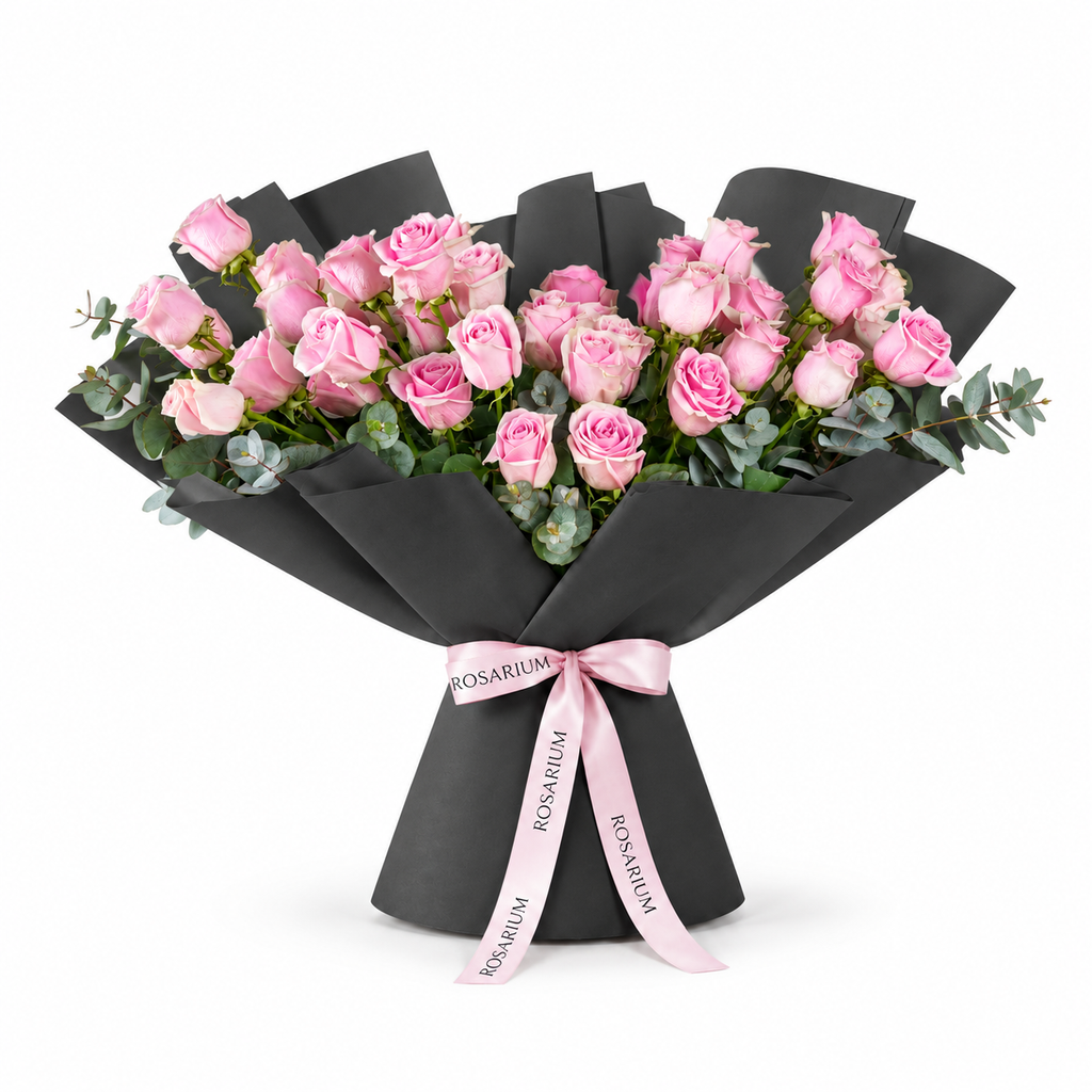 Wide bouquet of pink roses and eucalyptus in black wrapping with a Rosarium ribbon