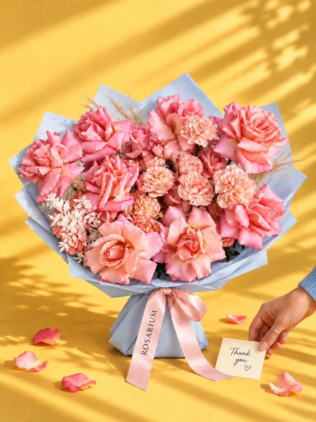 A bouquet of roses and carnations in shades of coral and pink, wrapped in blue paper.