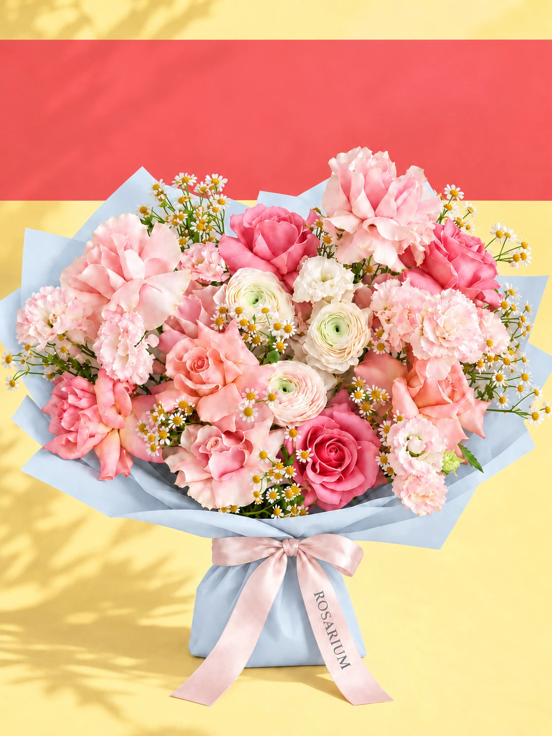 A bouquet of roses, carnations and lisianthus in shades of pink and cream, wrapped in blue paper.
