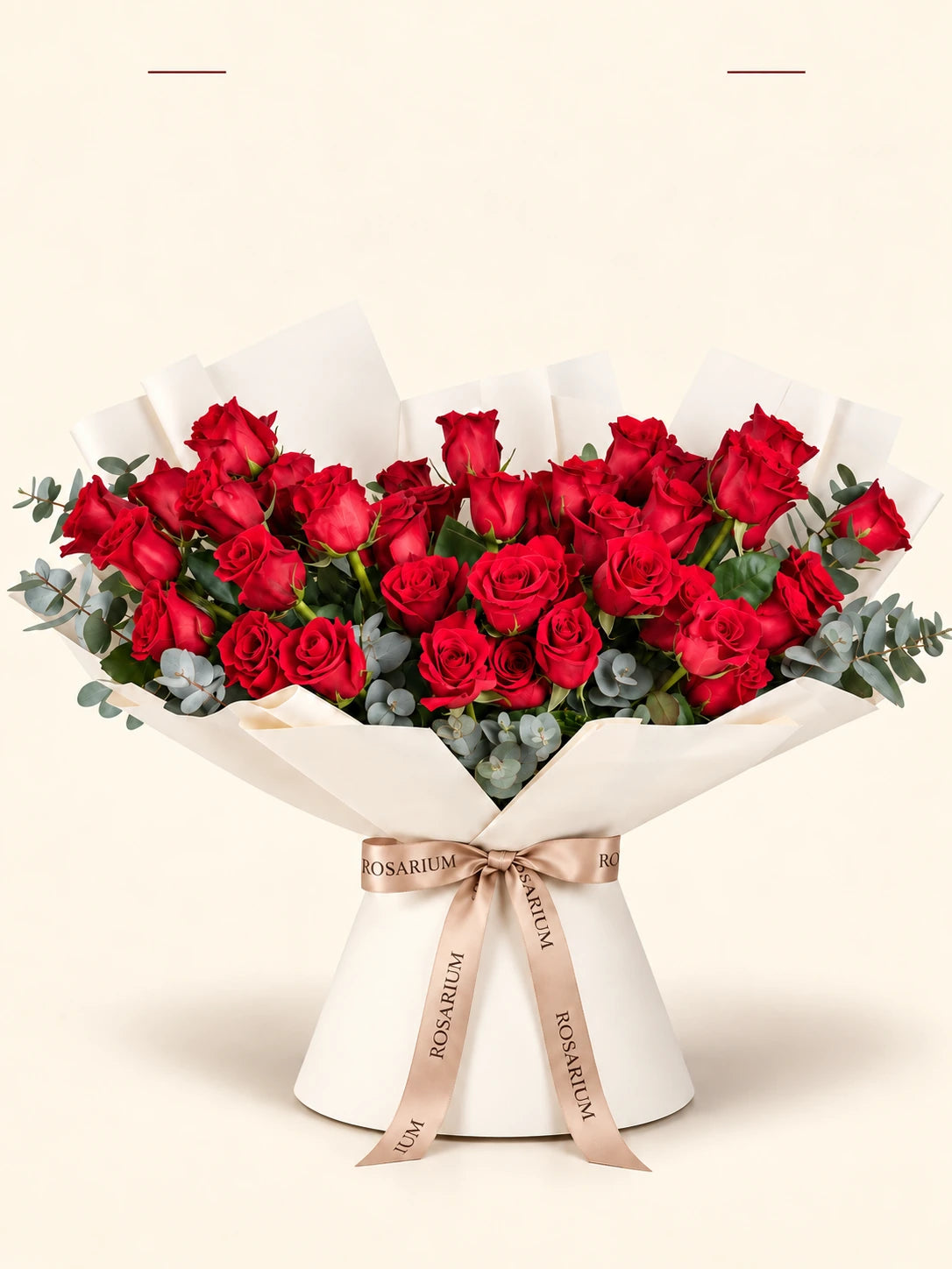 A bouquet of roses and eucalyptus in shades of red, wrapped in ivory paper.
