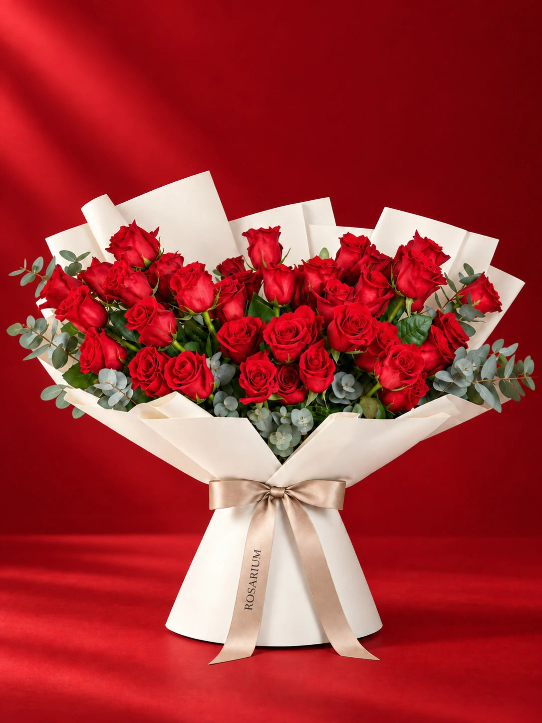 A bouquet of roses and eucalyptus in shades of red, wrapped in ivory paper.