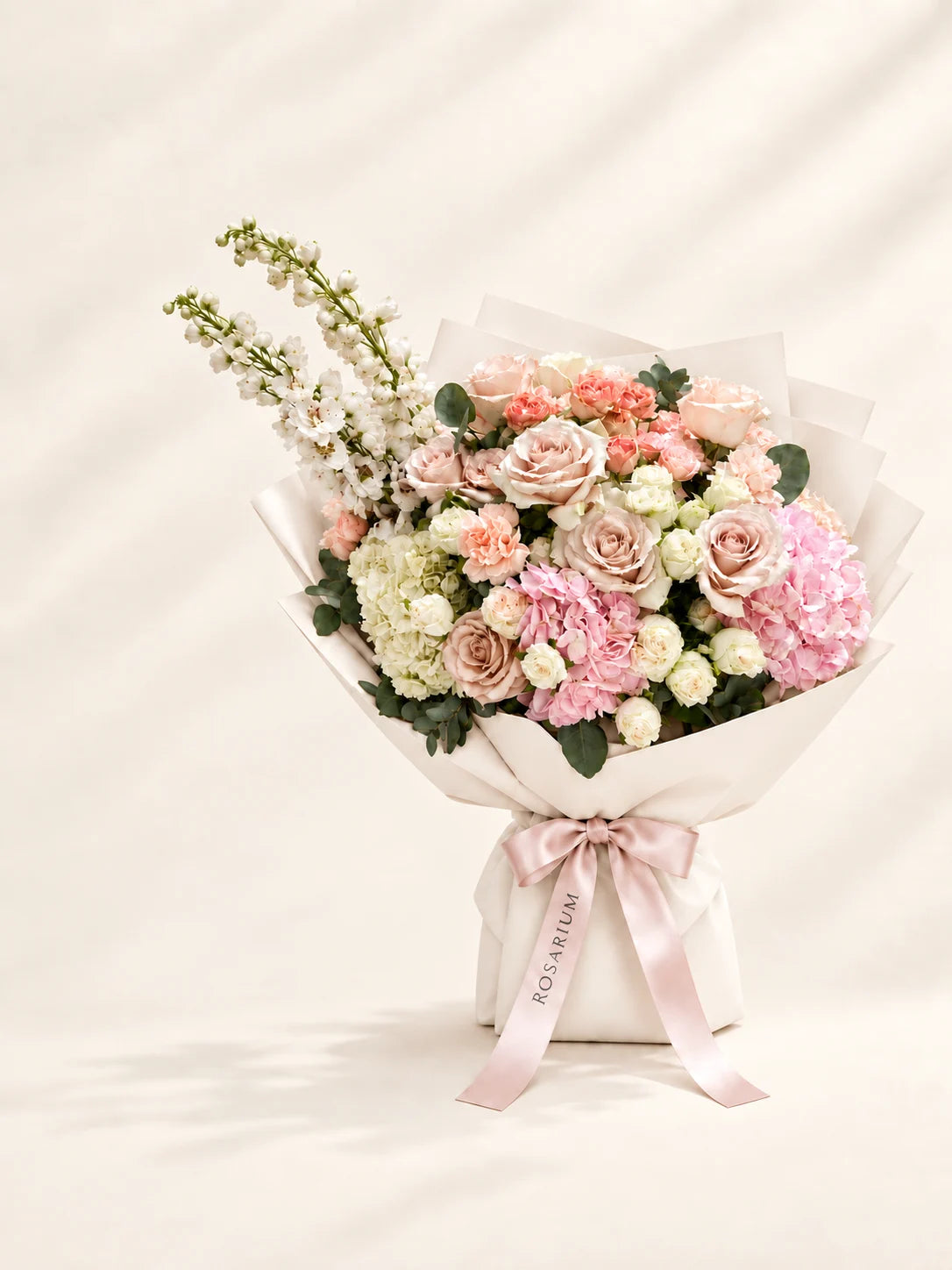 Pastel roses, pink and ivory hydrangeas and tall white blossoms in ivory wrapping with a blush Rosarium ribbon.